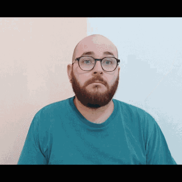 a bald man with glasses and a beard wears a blue shirt