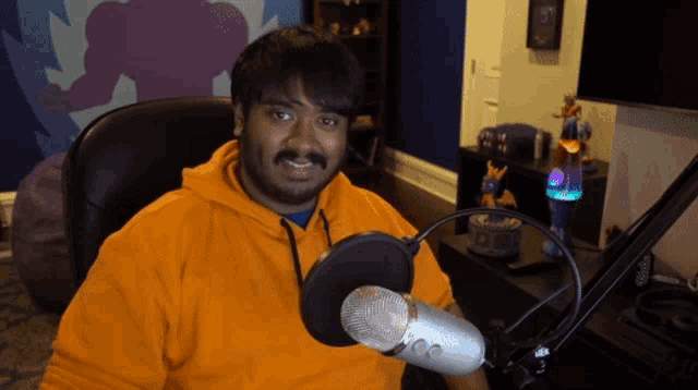 a man wearing an orange hoodie is sitting in front of a microphone and smiling