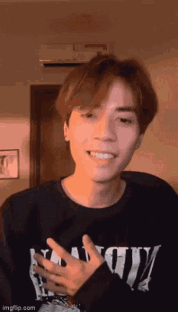 a young man wearing a black sweater is smiling and giving a peace sign .