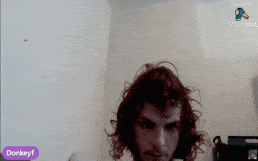 a man with curly hair is sitting in front of a white wall with a purple donkeyf sign in the corner