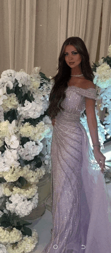 a woman in a long purple dress stands in front of a display of white flowers