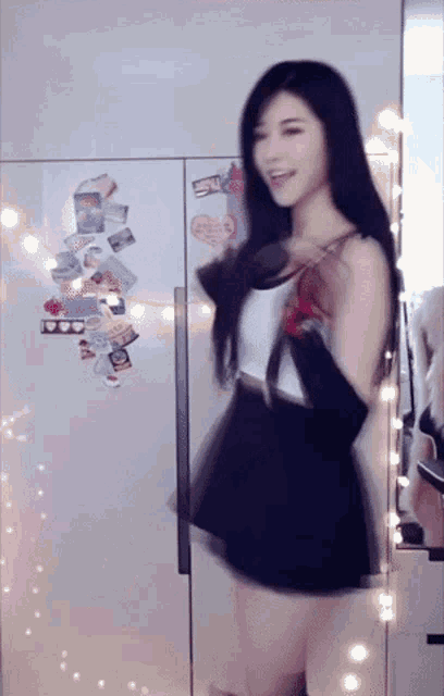 a woman in a black skirt is dancing in front of a refrigerator with stickers on it .