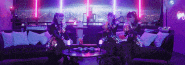 three girls are sitting on a couch in front of a neon sign that says ' a '
