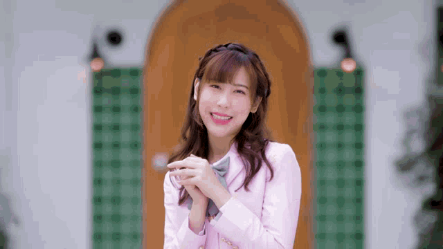 a girl in a pink jacket and bow tie is smiling with her hands folded