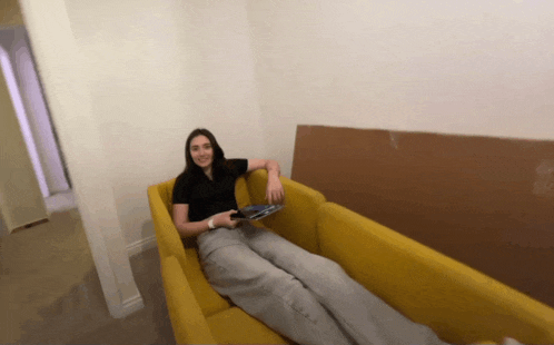 a woman sits on a yellow couch holding a controller