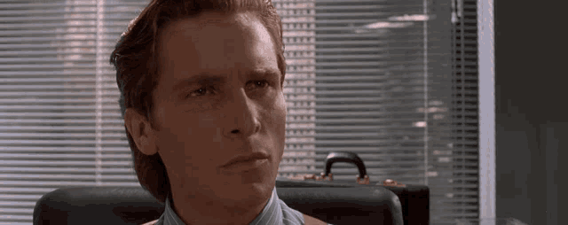 a man is sitting in front of a window with blinds on it