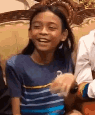 a young girl is sitting on a couch and smiling while holding a piece of paper .