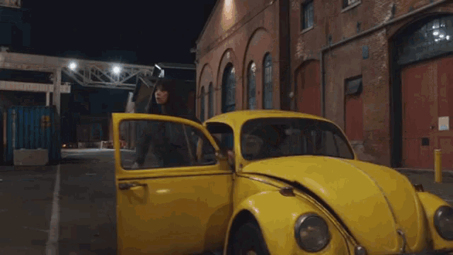 a woman is standing next to a yellow car with its door open