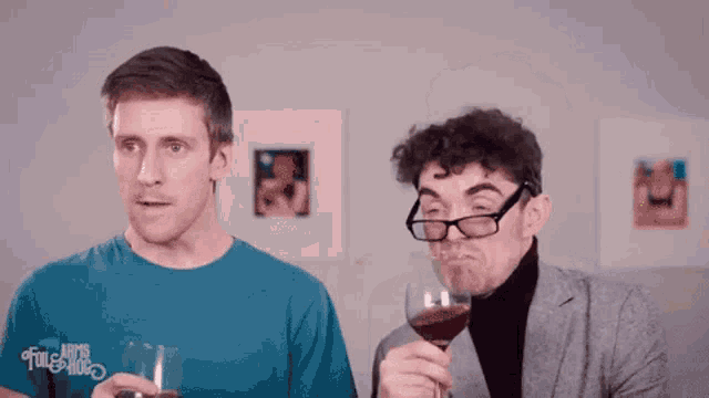 a man in a blue shirt holds a glass of wine next to another man in a suit