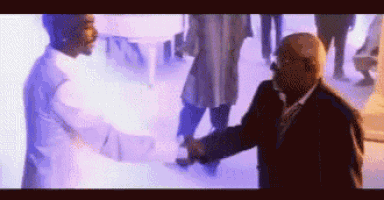 a man in a suit and tie shakes hands with another man in a white shirt