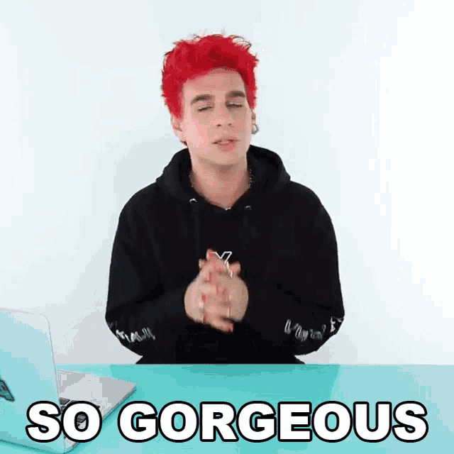 a man with red hair is sitting at a desk with his hands folded and the words so gorgeous above him