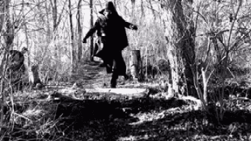 a black and white photo of a man and woman running through a forest .