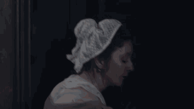 a woman wearing a white hat stands in front of a dark door