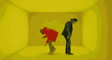 a man in a red jacket and a man in a black suit are standing in a yellow room .