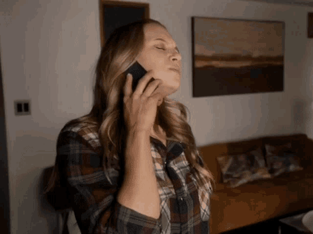 a woman wearing a plaid shirt is talking on a cell phone