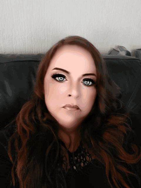 a woman with long hair and blue eyes is sitting on a black leather couch