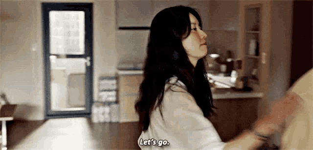 a woman is standing in a kitchen talking to a man and says `` let 's go . ''