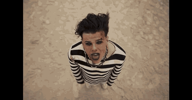 a man in a striped shirt with black eyes is standing in the sand .