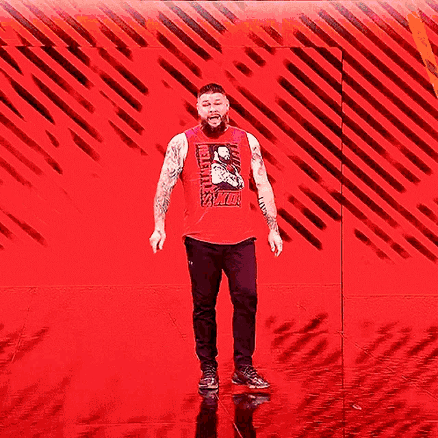 a man in a red tank top is standing in front of a red background that says kevin owens