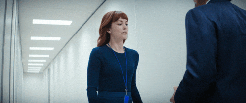 a woman wearing a blue lanyard talks to a man in a suit