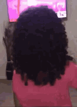 a little girl with curly hair is sitting in front of a pink television .