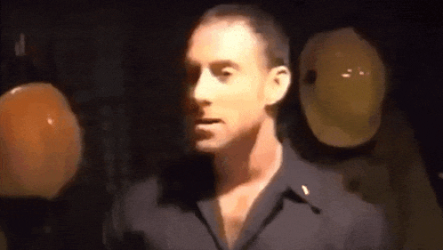 a man in a black shirt is standing in a dark room with balloons in the background .