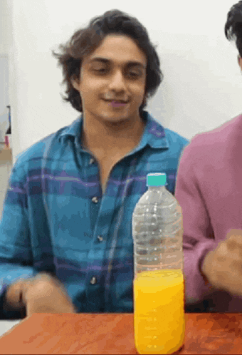 a man in a plaid shirt sits at a table with a bottle of orange juice in front of him