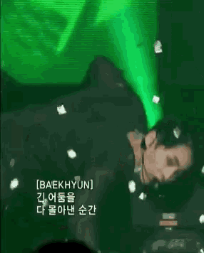 a man is laying on a stage with a green light behind him and flowers falling around him .