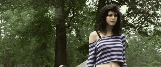 a woman in a striped crop top is standing in a forest