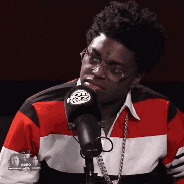 a man wearing glasses and a red , white and blue shirt is sitting in front of a microphone .