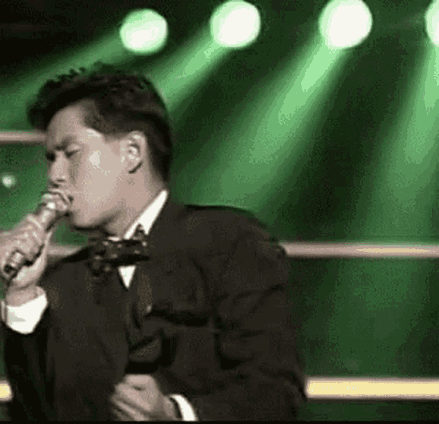 a man in a suit and bow tie is singing into a microphone on stage .