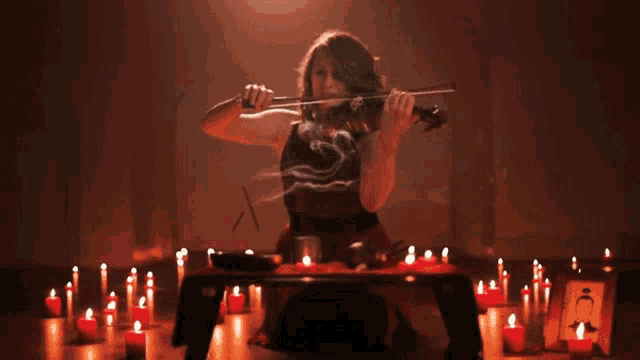 a woman playing a violin in a dark room with candles