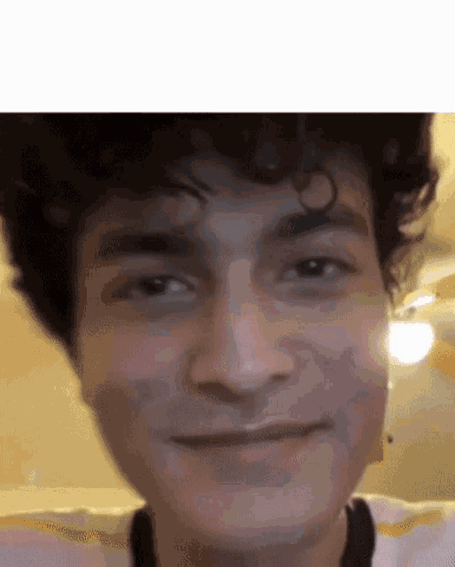 a close up of a man 's face with curly hair and a ceiling fan in the background .