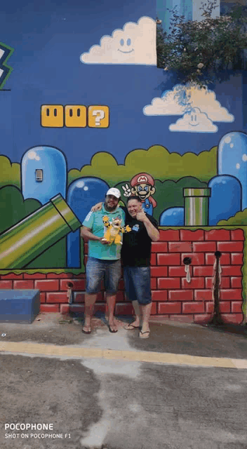 two men are posing in front of a mario mural on a wall
