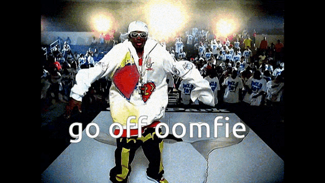 a man is standing on a stage in front of a crowd with the words go off oomfie on the bottom