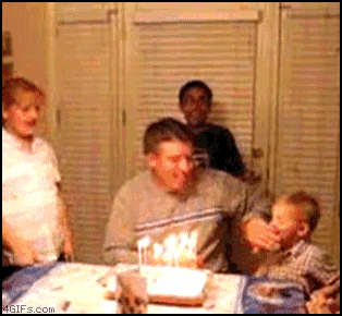 a man blows out candles on a birthday cake while a child watches