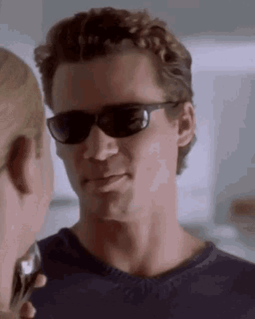 a man wearing sunglasses is looking at a woman while holding a glass of wine .