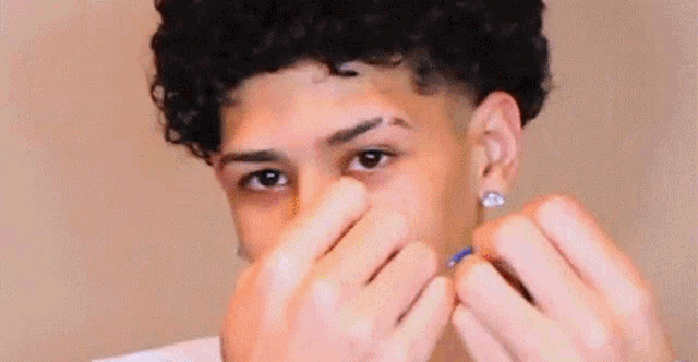 a young man with curly hair is cleaning his nose with a cotton swab .