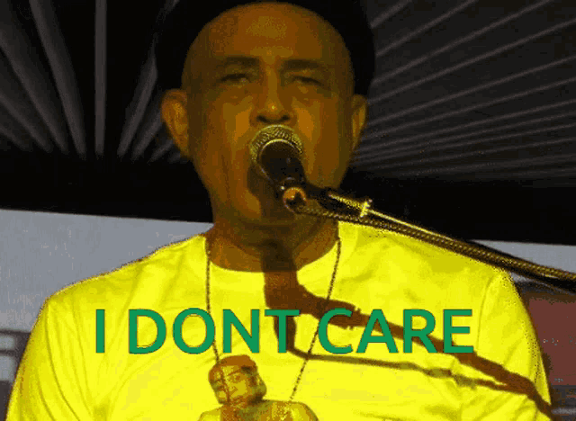 a man singing into a microphone while wearing a yellow shirt that says i don t care