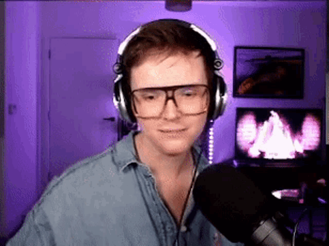 a young man wearing headphones and glasses is talking into a microphone .