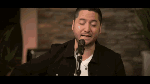 a man in a black jacket singing into a microphone with his eyes closed