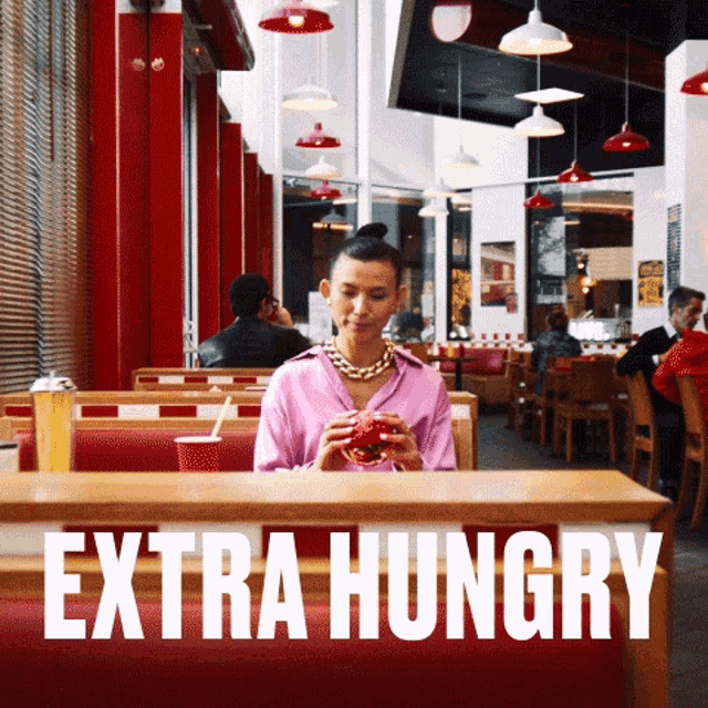 a woman is sitting at a table in a restaurant with the words extra hungry written above her