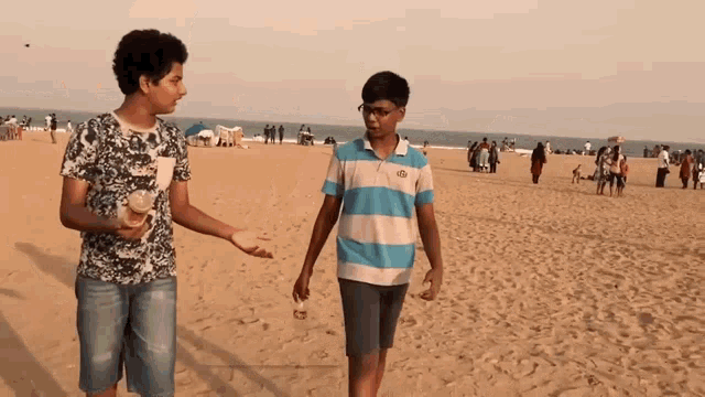 two boys walking on a sandy beach with one wearing a shirt that says ' abercrombie & fitch '