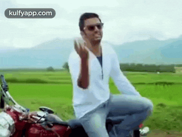 a man is sitting on a red motorcycle in a field and giving the middle finger .