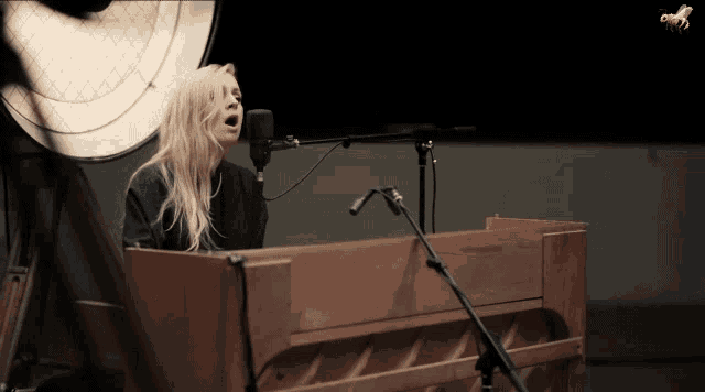 a woman is singing into a microphone while playing a piano