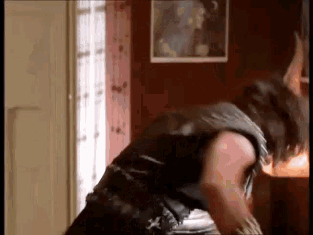 a man in a leather vest is sitting on a couch in a room .
