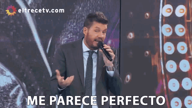 a man in a suit and tie singing into a microphone with the words me parece perfecto behind him