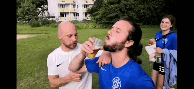 a man with a beard is drinking beer from a glass while standing next to a woman .