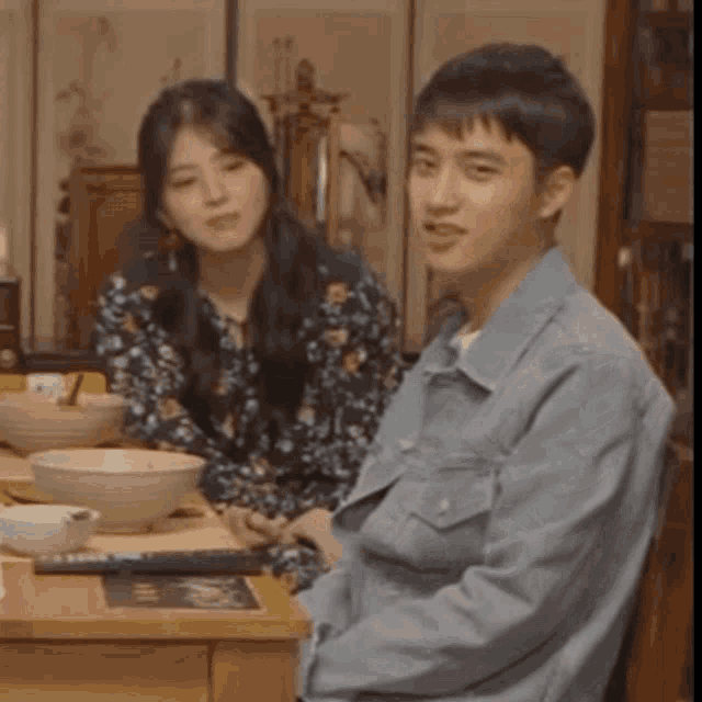 a man and a woman are sitting at a table with bowls of food on it .