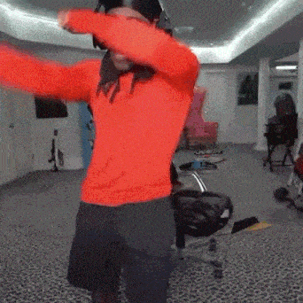 a man wearing a red sweater and black shorts is dancing in a room .